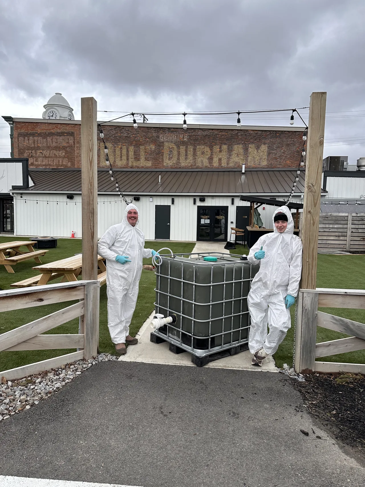 Two EvE Waste team members in white protective suits standing on either side of the AD system prototype, a pallet-mounted tank installed outdoors.